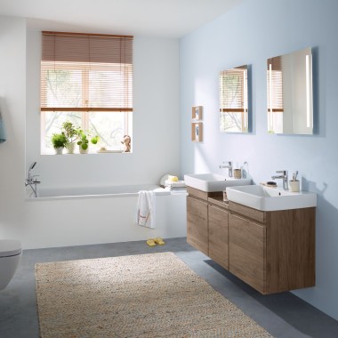 Bagno per famiglia con parete azzurra e mobili da bagno in legno di noce, mobile specchio, placca di comando e sanitari in ceramica di Geberit