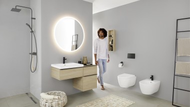Persona che entra in un bagno con lavabo, vaso WC, bidet e mobili bagno della serie Geberit iCon